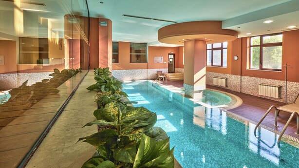 An indoor swimming pool with clear water, surrounded by walls with a beige and brown color scheme, and a glass barrier on one side. - Yantra Grand Hotel -sharlopov Hotels (Veliko Tarnovo)