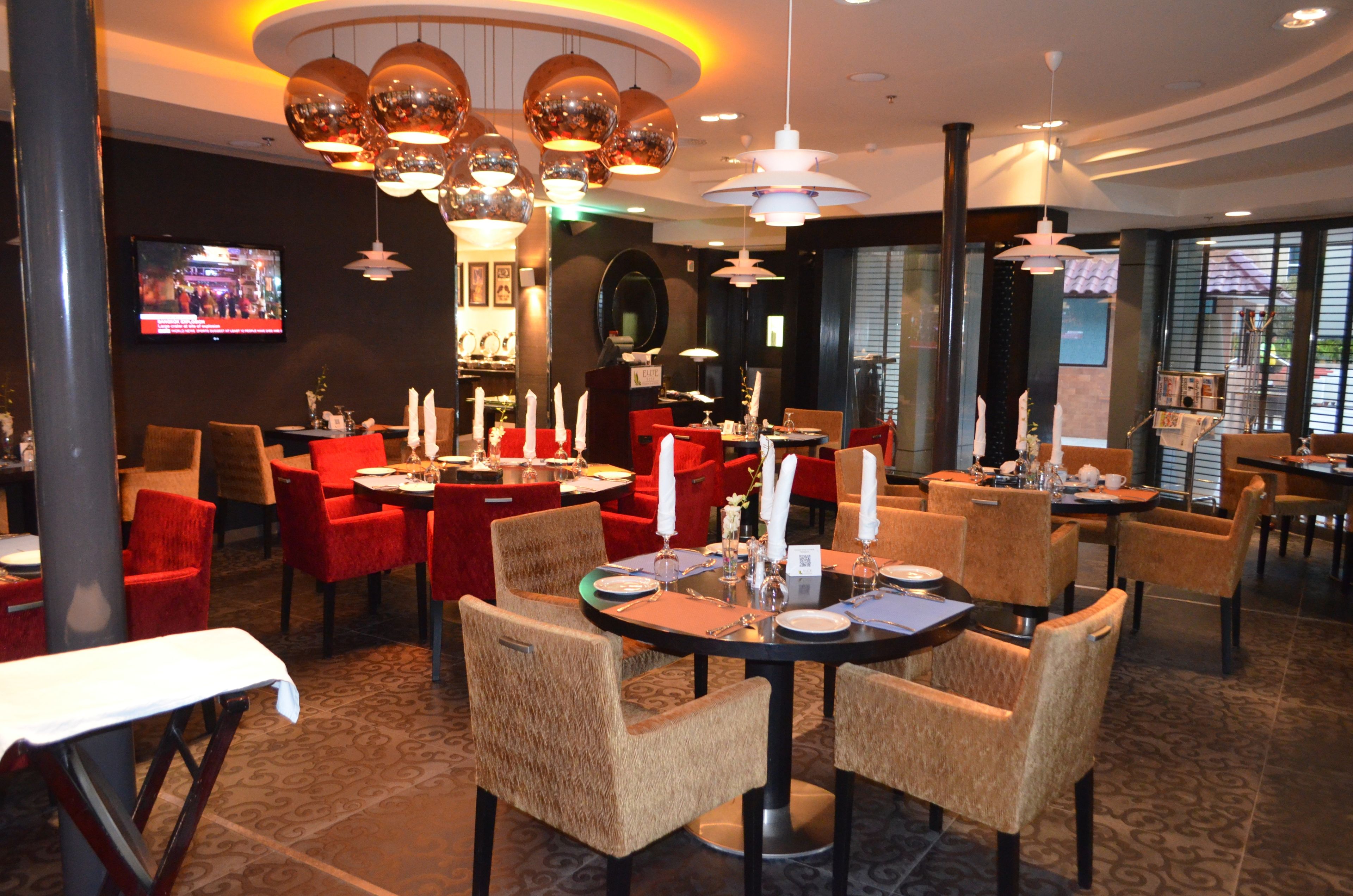A restaurant with round tables, red chairs, and a TV mounted on the wall.