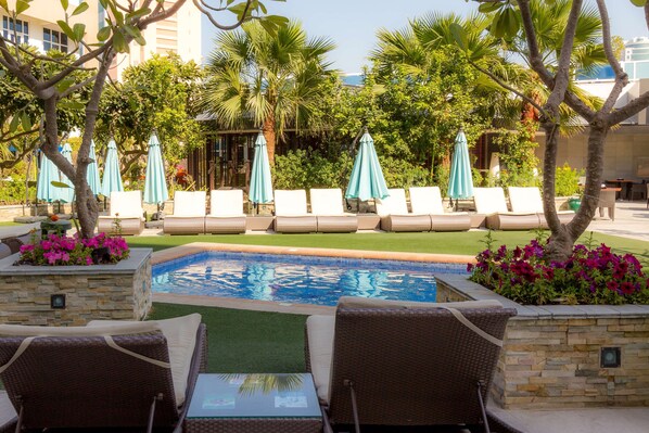 A pool area with lounge chairs and umbrellas, surrounded by greenery and a stone wall. - Elite Seef Residence & Hotel (Manama)