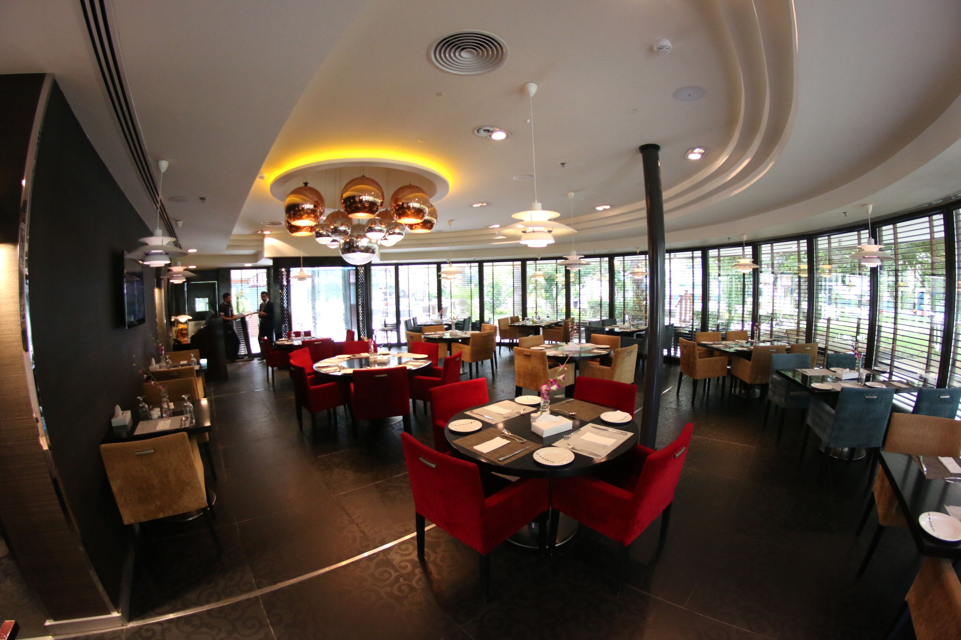A modern restaurant with round tables, red chairs, and large windows.