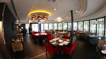 A modern restaurant with round tables, red chairs, and large windows.