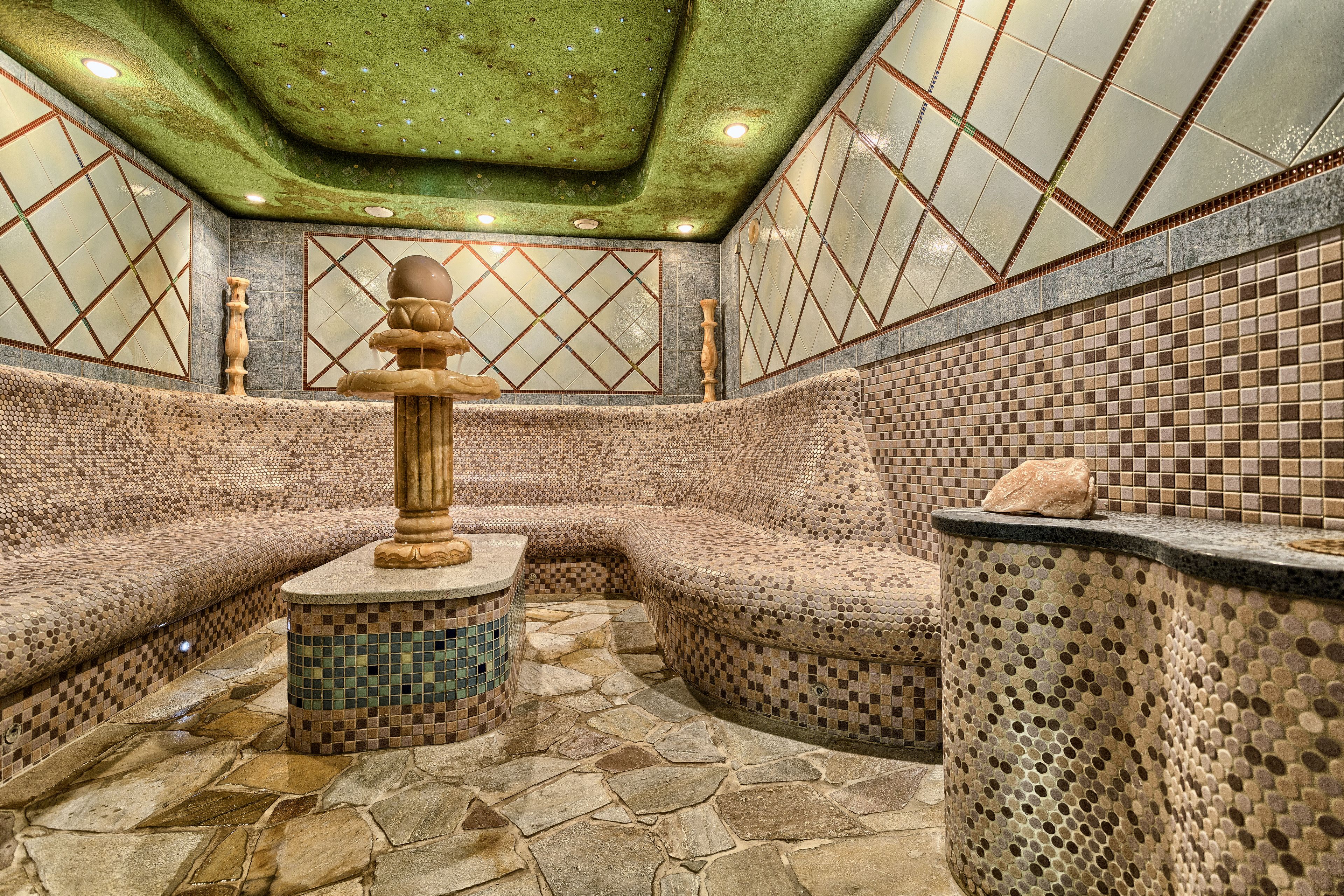 A spa area with mosaic tiled walls, a stone floor, and a central column.