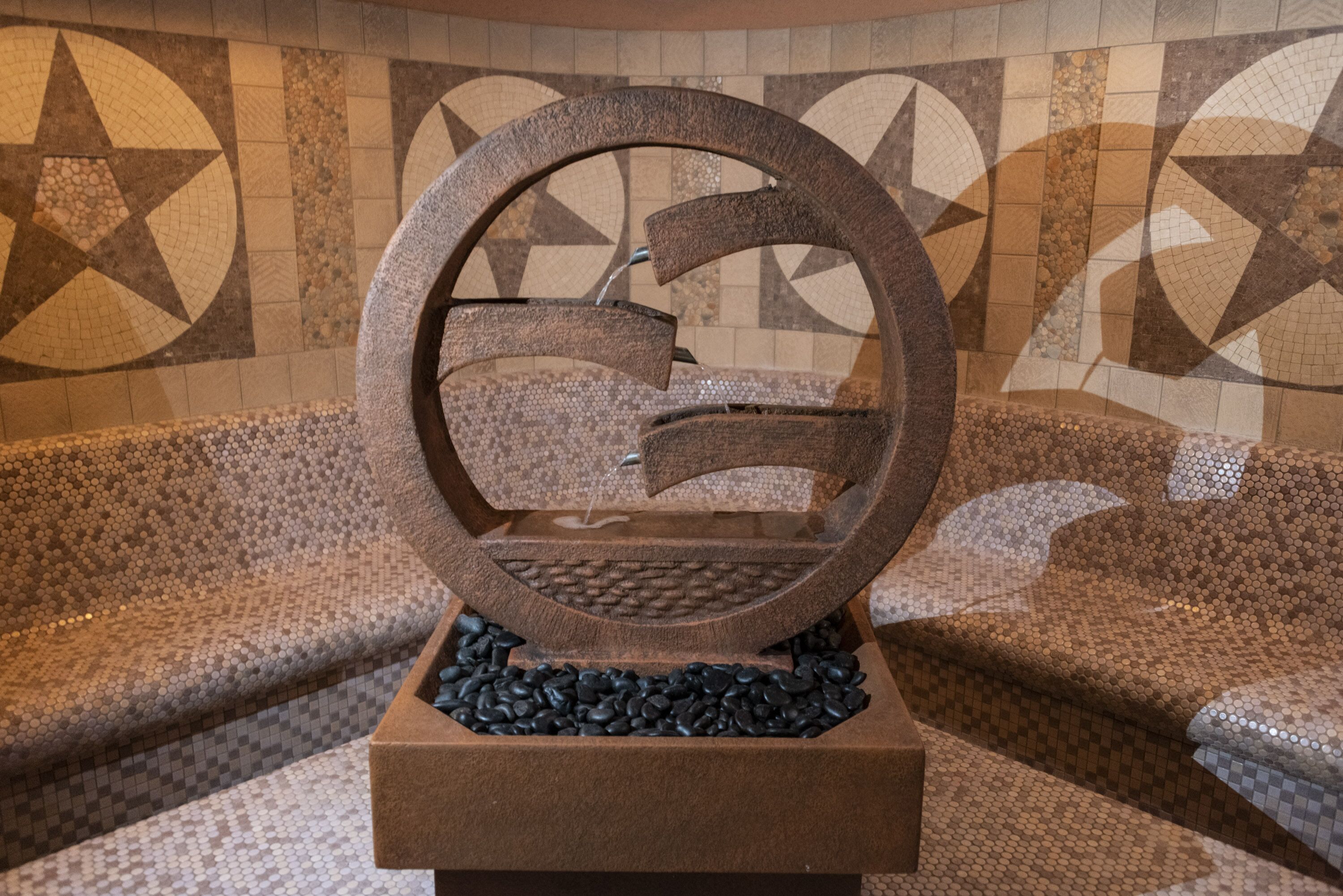 A stone fountain with a circular design, set on a tiled floor with geometric patterns.