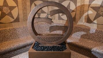 A stone fountain with a circular design, set on a tiled floor with geometric patterns.