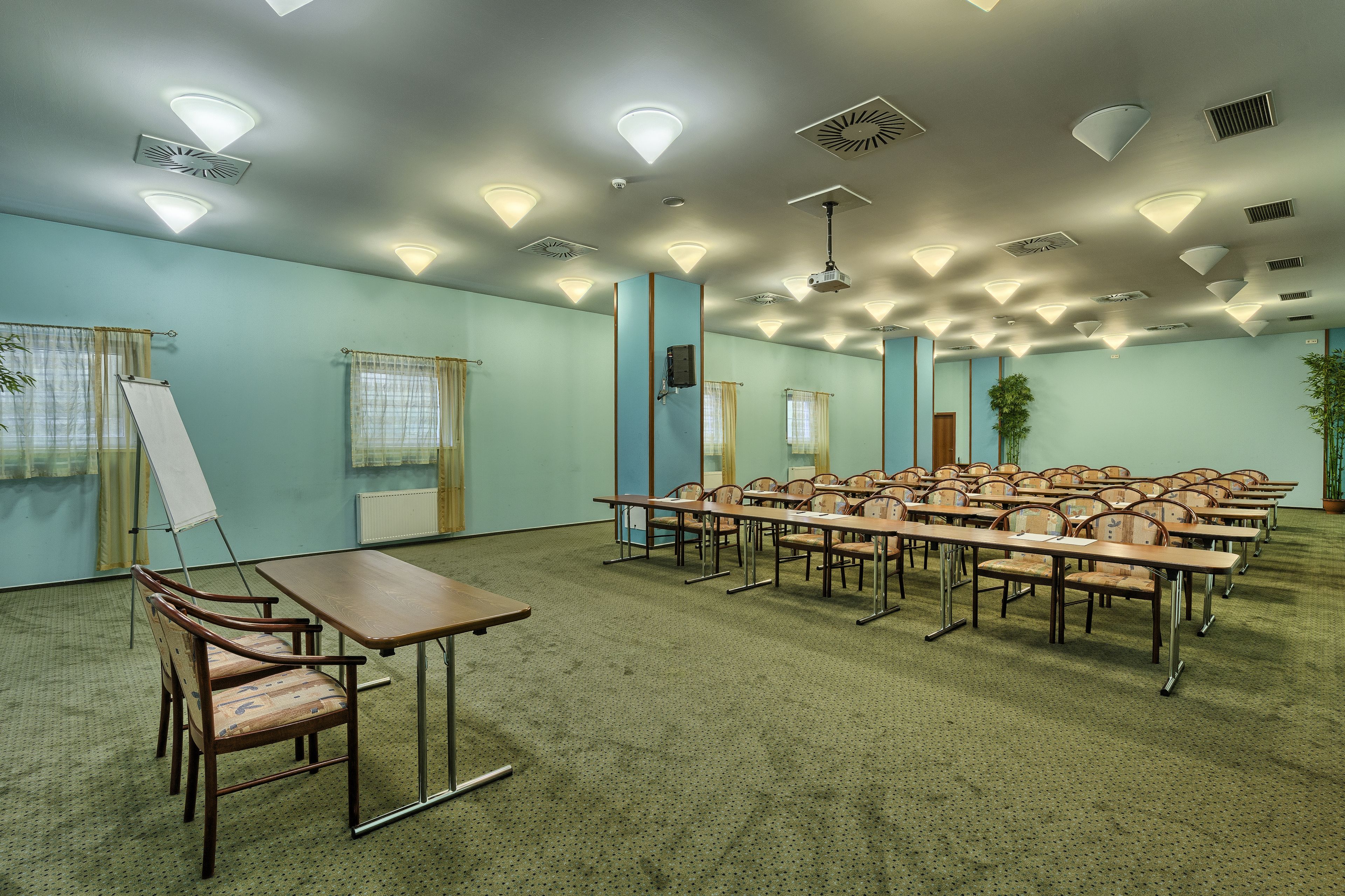 A conference room with multiple tables and chairs, ceiling lights, and a large window with curtains.