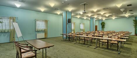 A conference room with multiple tables and chairs, ceiling lights, and a large window with curtains.