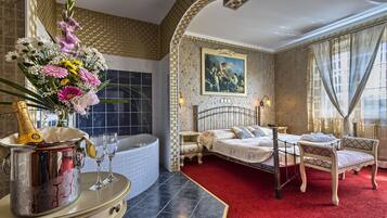 Habitación de hotel con alfombra roja, cama, mesita de noche, silla, un cuadro en la pared y un florero con flores.