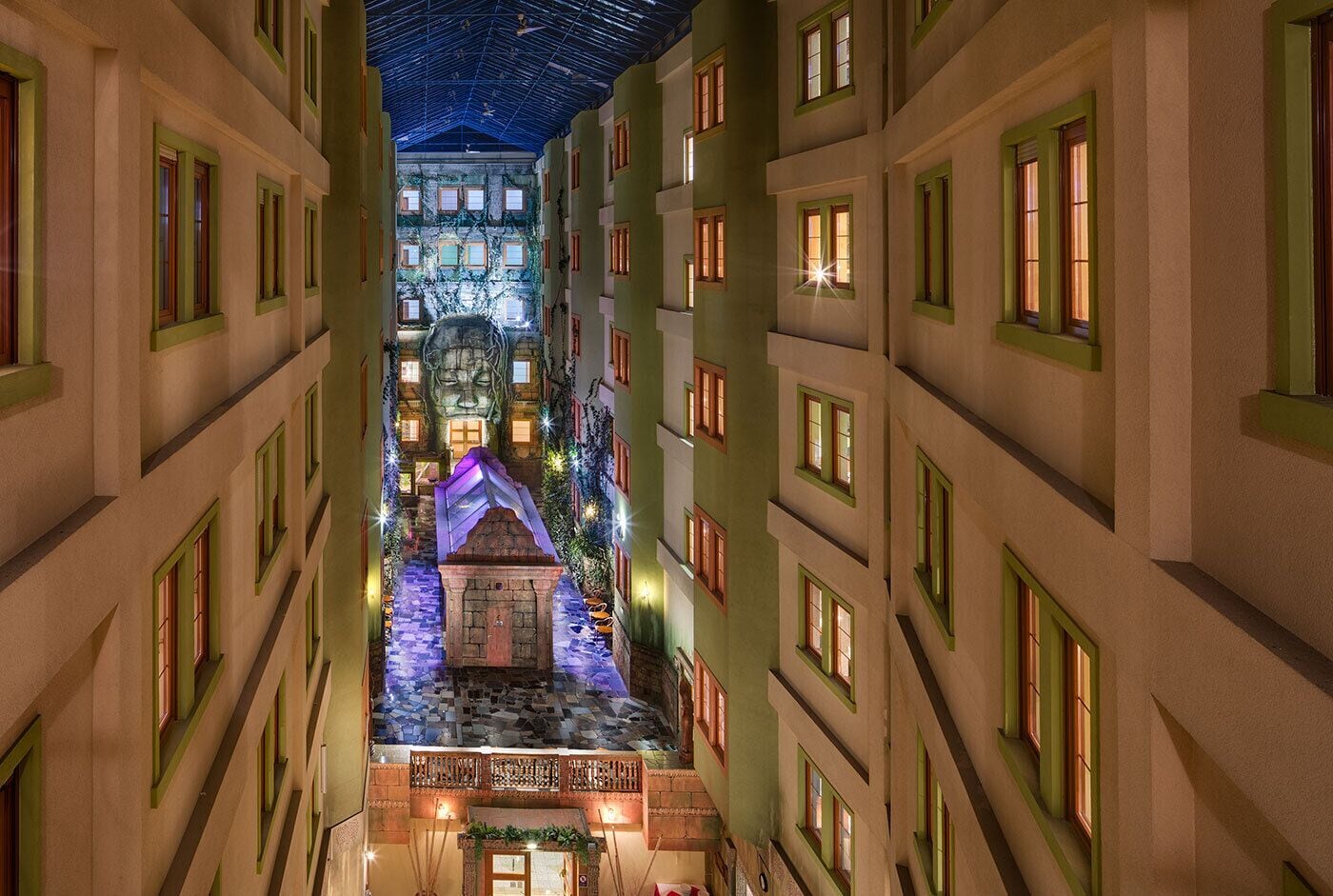 Pasillo de hotel con varios pisos, una escalera central y una zona decorativa con una estatua.