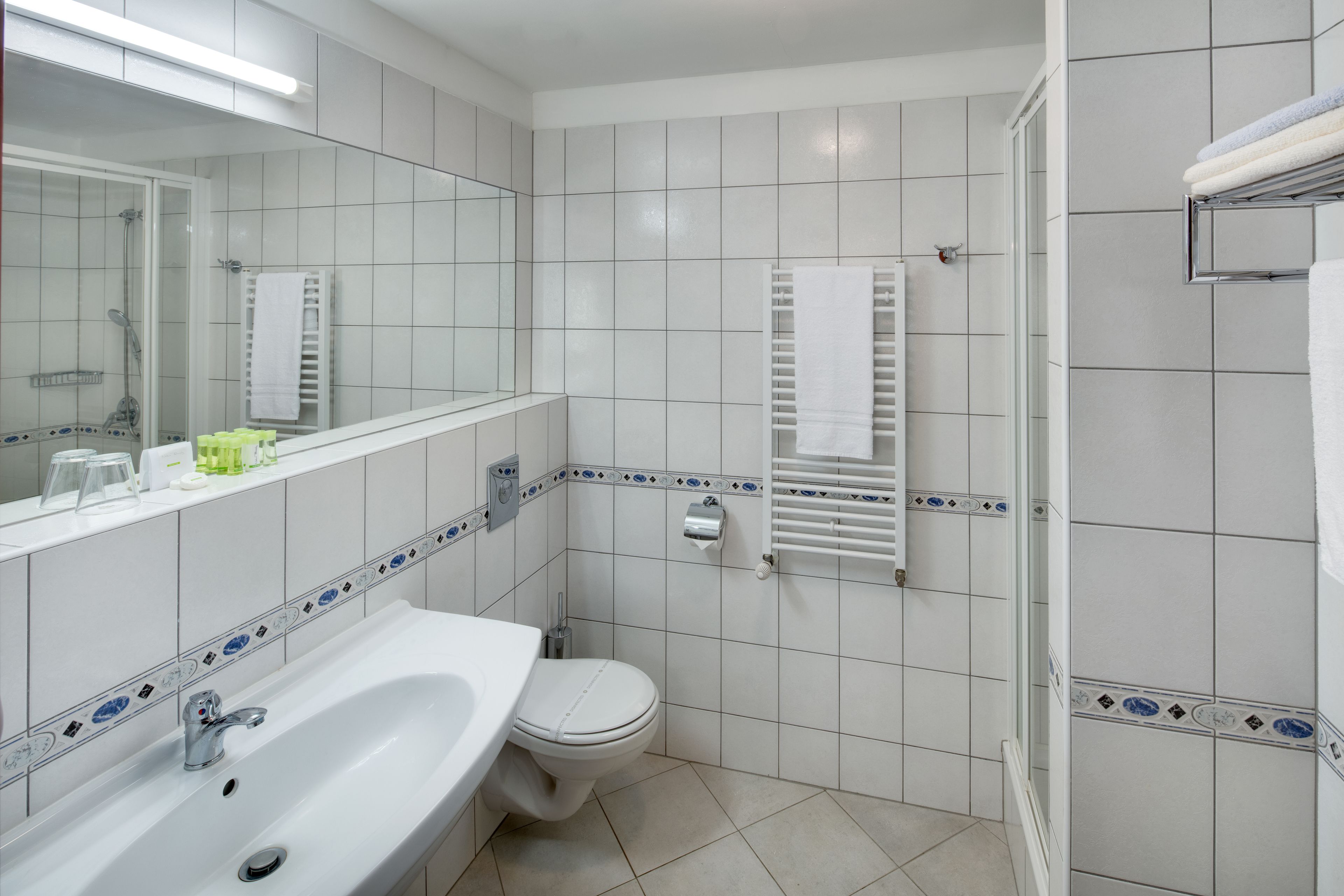 A bathroom with a white sink, toilet, and shower. There are towels hanging on a rack and a mirror above the sink.