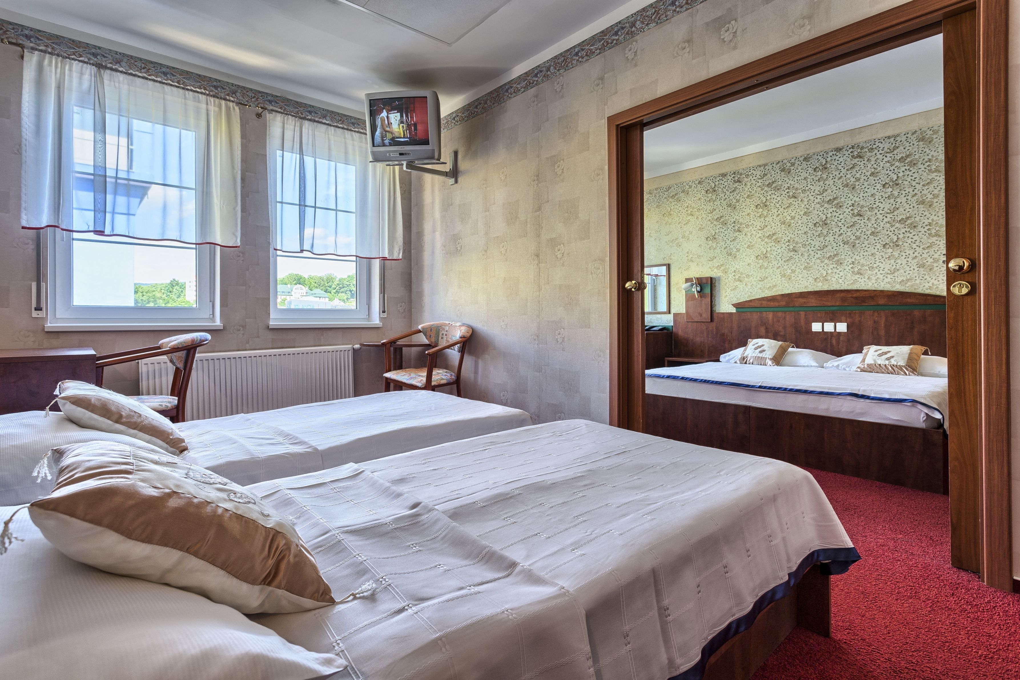Habitación de hotel con dos camas, una silla de madera, un televisor y un espejo.