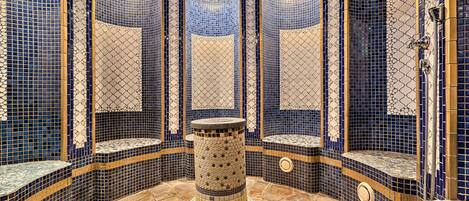 Un área de spa con paredes de mosaicos, una columna central y suelo de piedra.
