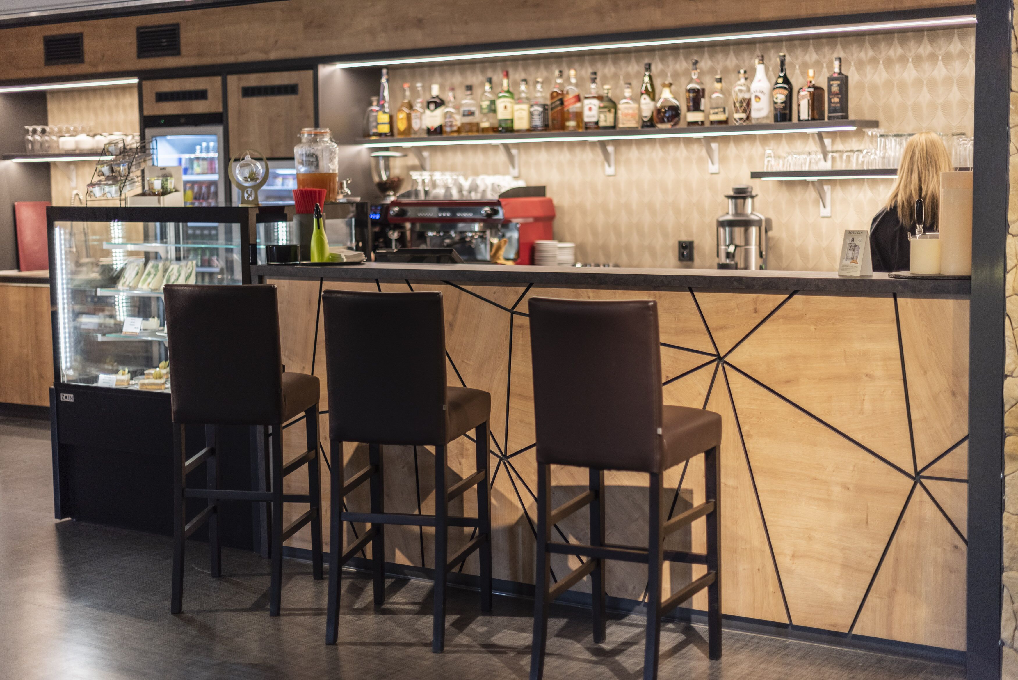 A bar area with stools, a refrigerator, and shelves with bottles.