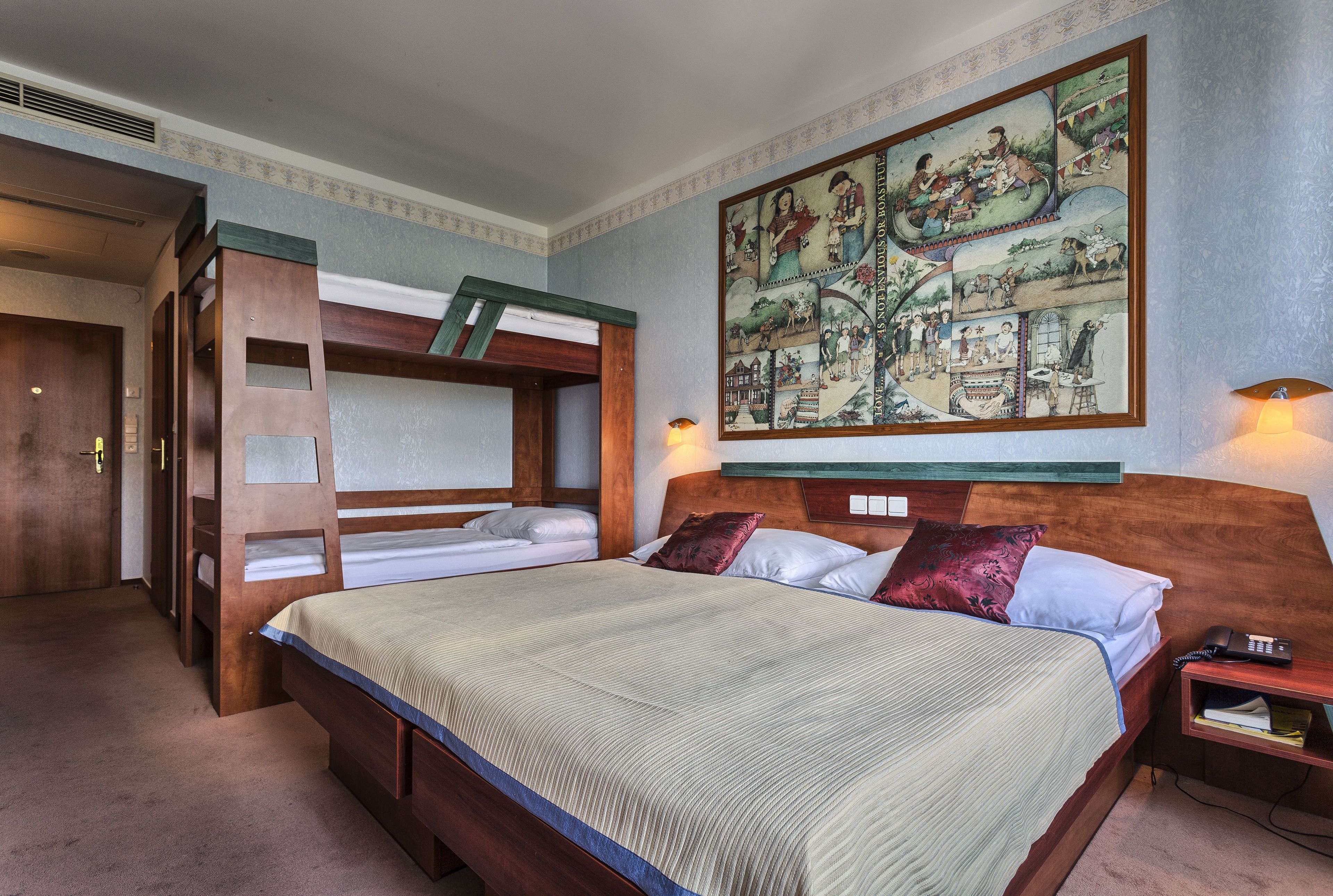 A hotel room with a large bed, a bunk bed, a painting on the wall, and a bedside table with a lamp.