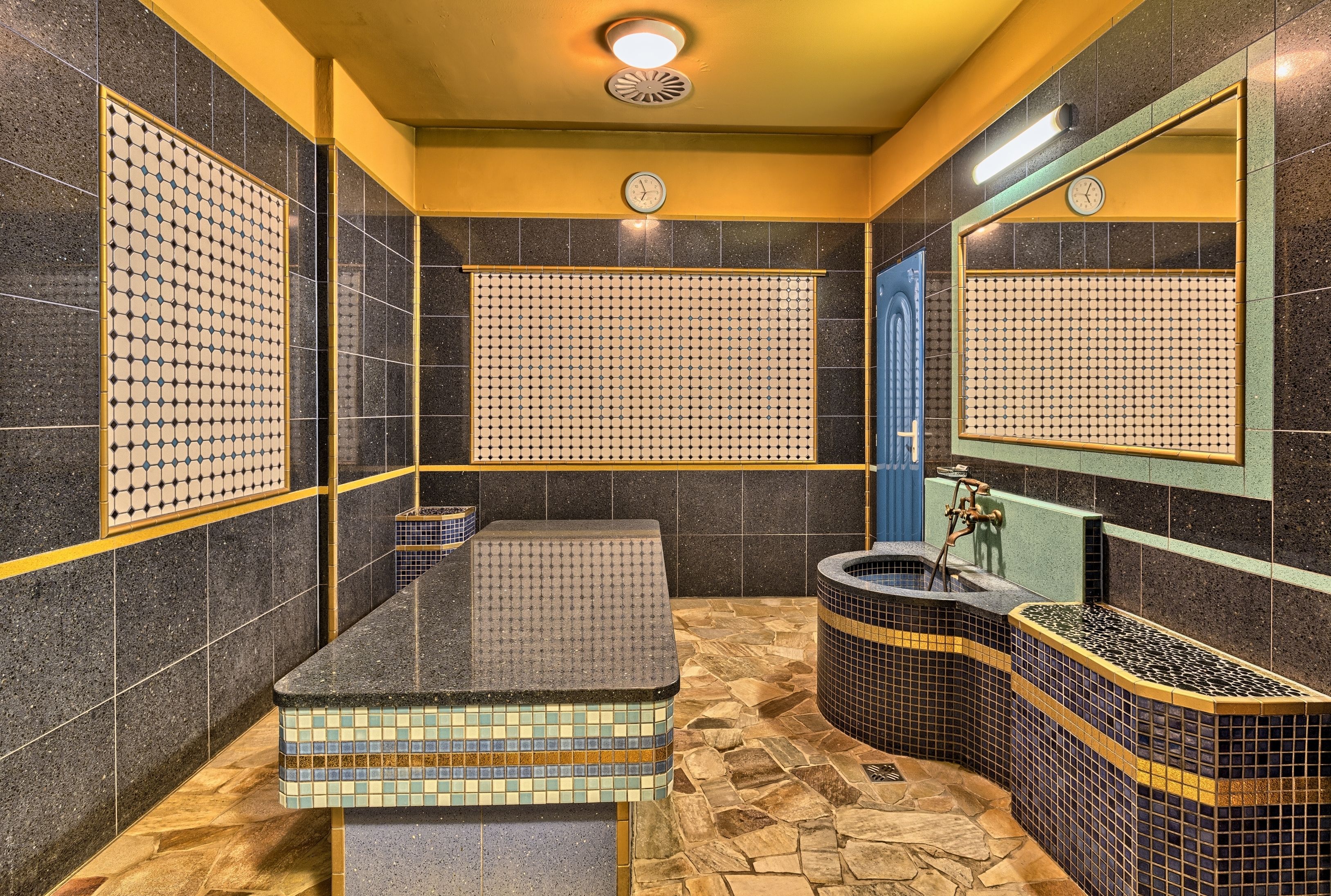 A bathroom with a tiled floor, a sink, a mirror, and a clock on the wall.