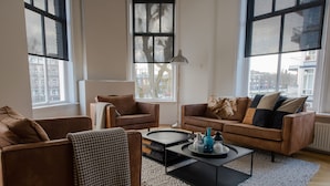Un salón moderno con sofás de cuero, una mesa de centro y un amplio ventanal con vistas a edificios.