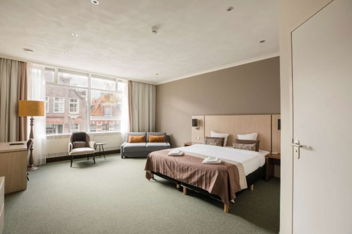 Une chambre d’hôtel équipée d’un lit, d’un bureau, d’une chaise et d’une fenêtre donnant sur des immeubles.