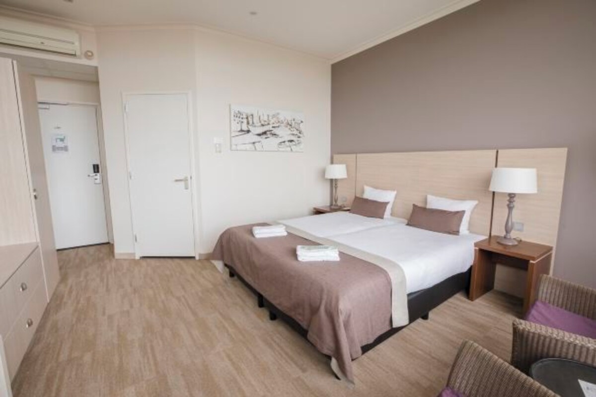 Une chambre d’hôtel avec un lit, des tables de chevet, une chaise, un tableau au mur et une porte.