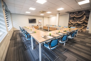 A conference room with a long table, blue chairs, and a projector screen.