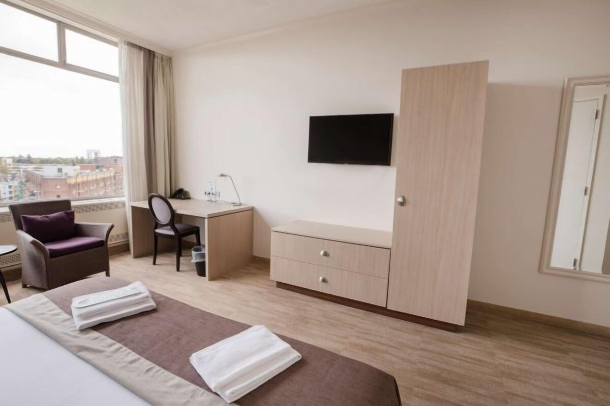A hotel room with a bed, a desk, a chair, a TV, and a wardrobe.