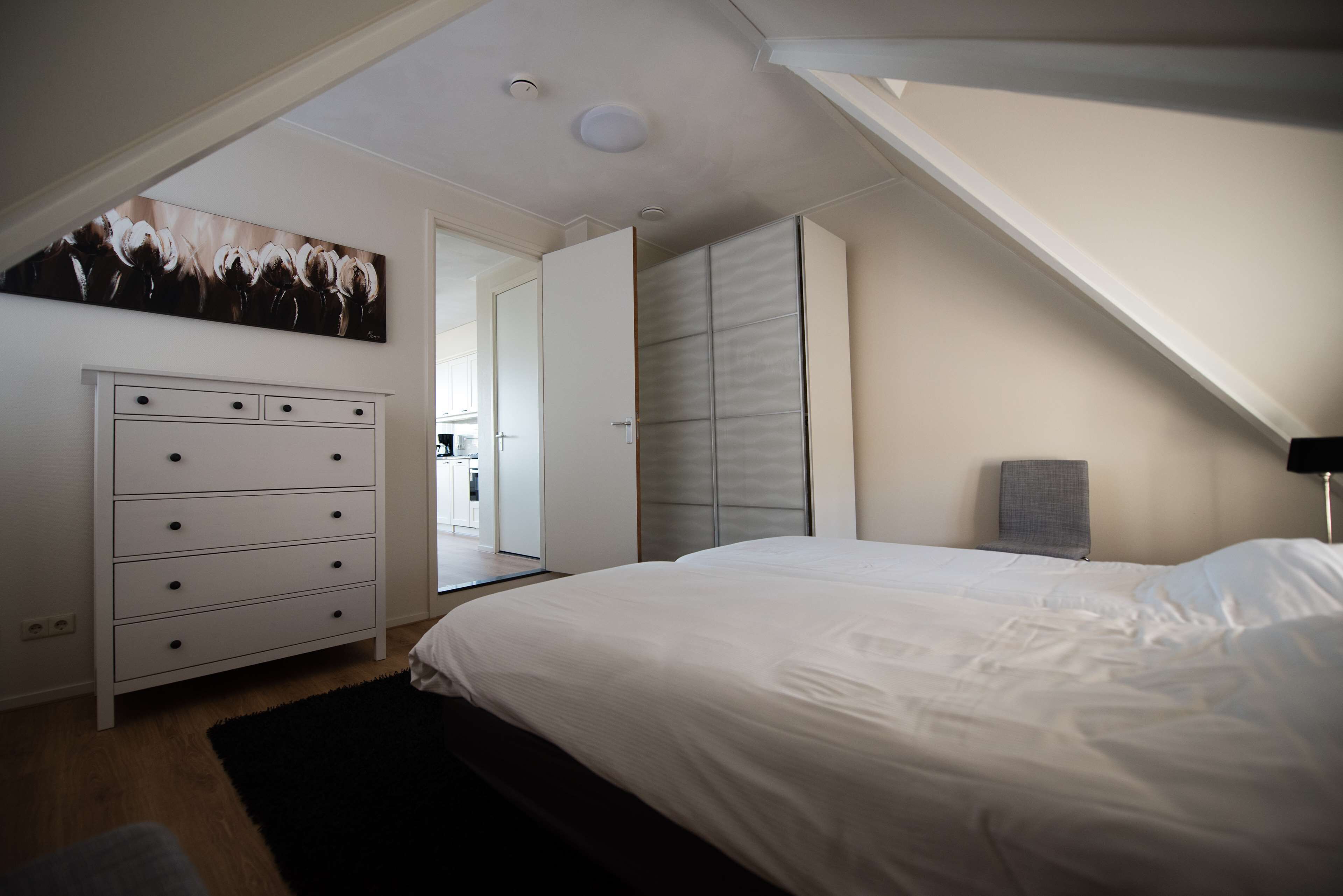 Ein Schlafzimmer mit einem Bett, einem Schminktisch, einem Gemälde und Blick auf die Küche.