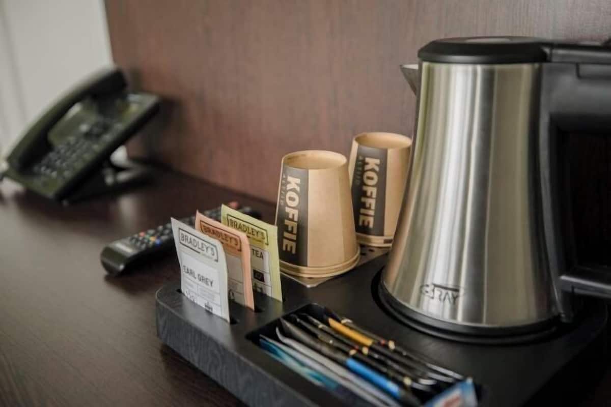 A coffee station with a kettle, cups, and a phone on a desk.
