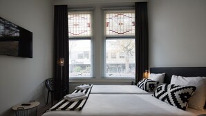 A hotel room with two beds, a flat-screen TV mounted on the wall, a small round table with a chair, and a window with decorative glass panes. - Flonk Hotel Groningen Centre, BW Signature Collection (Groningen)
