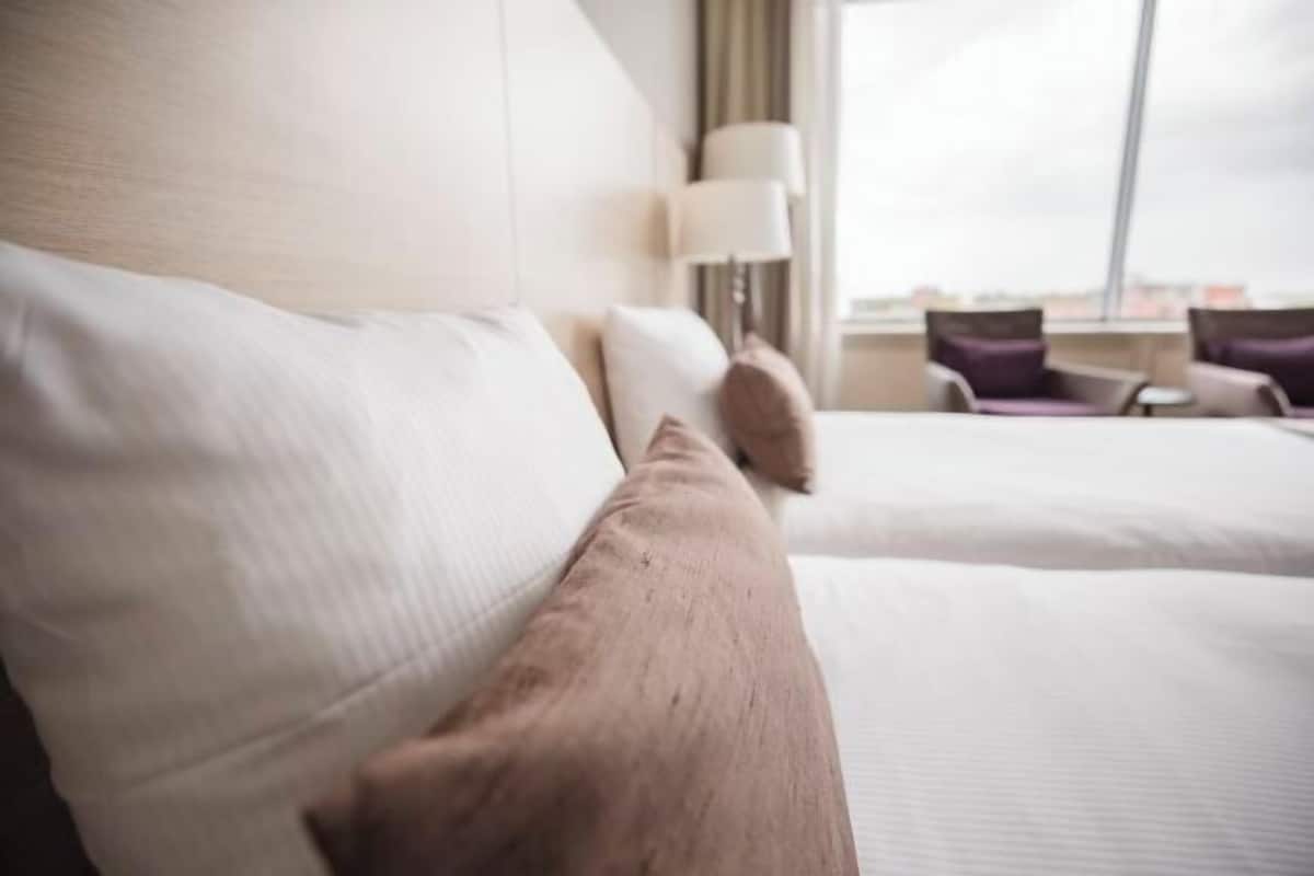 A hotel room with two beds, a lamp, and a view of the city.