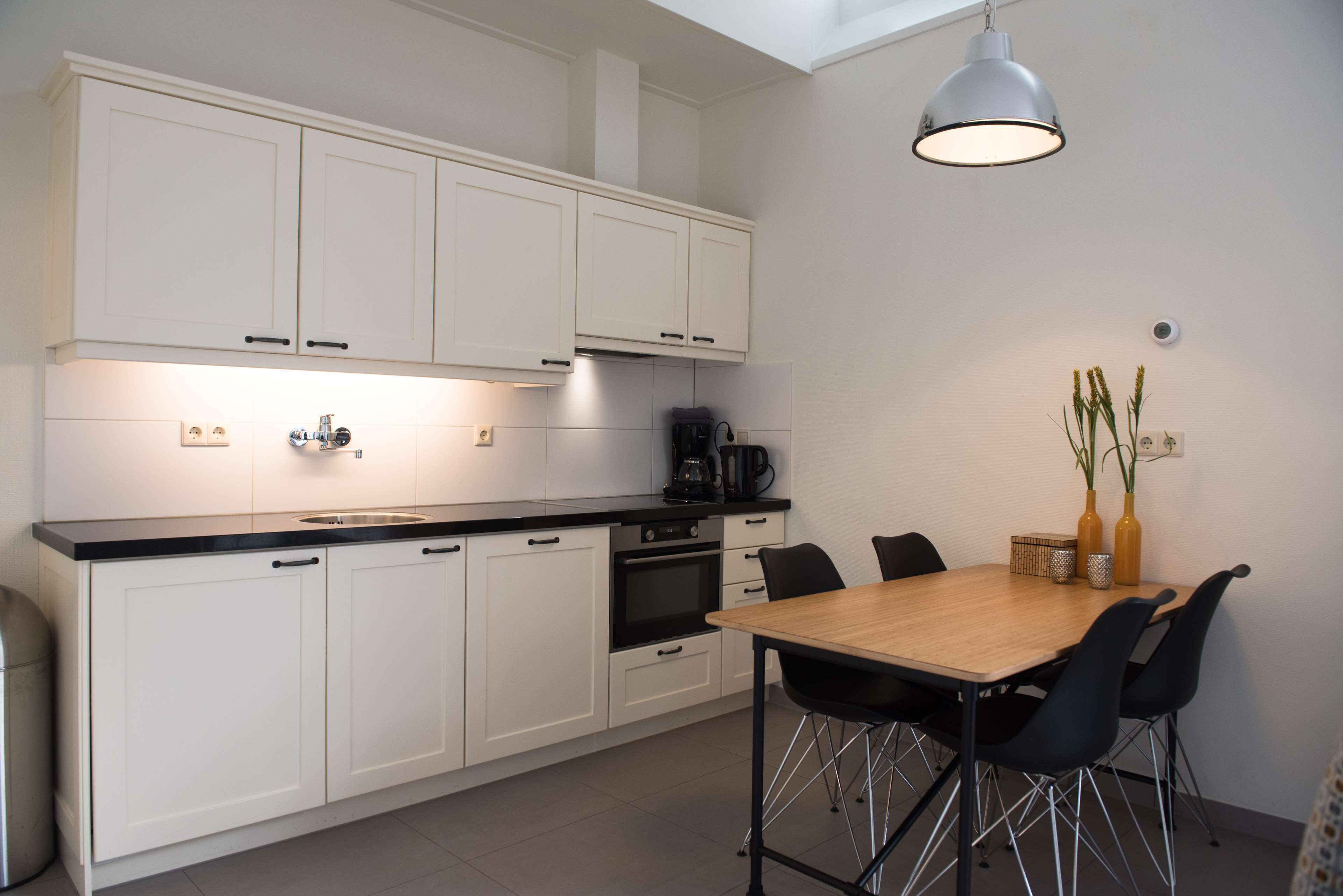 A modern kitchen with white cabinets, a black countertop, and a dining area with a wooden table and black chairs.