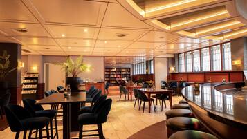 A modern hotel lobby with a bar area, seating arrangements, and a large bookshelf.