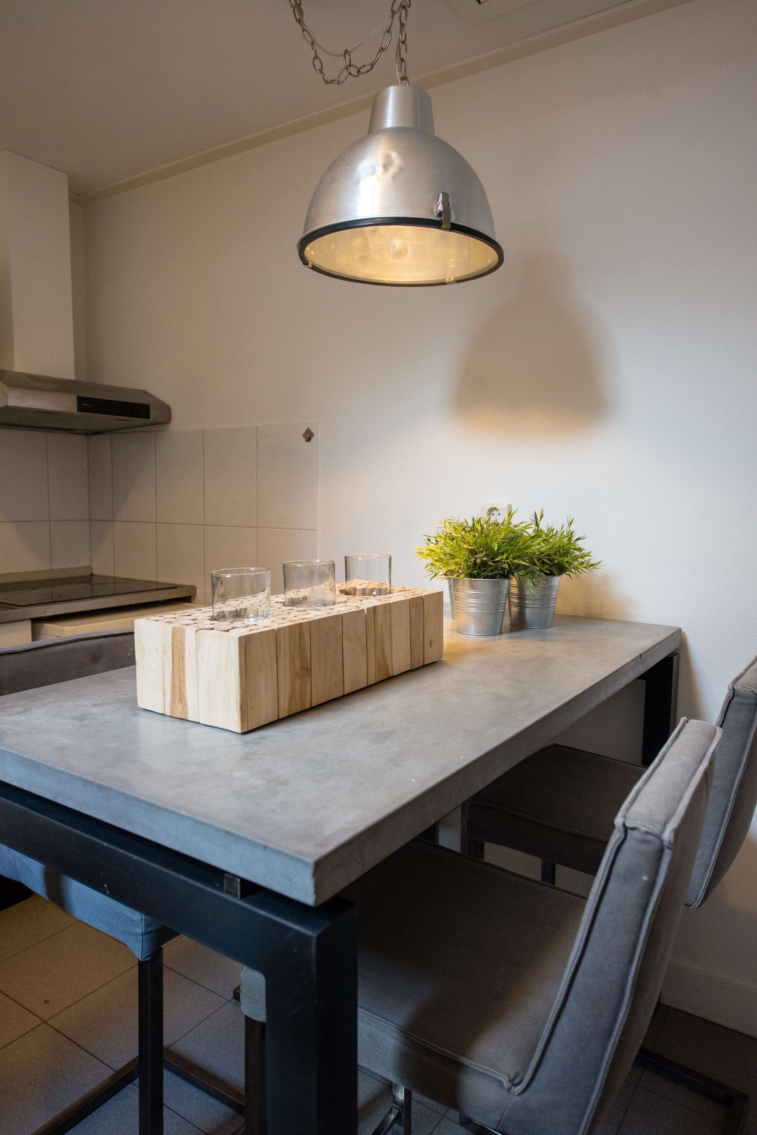 A kitchen with a large table, a hanging light fixture, and a potted plant.