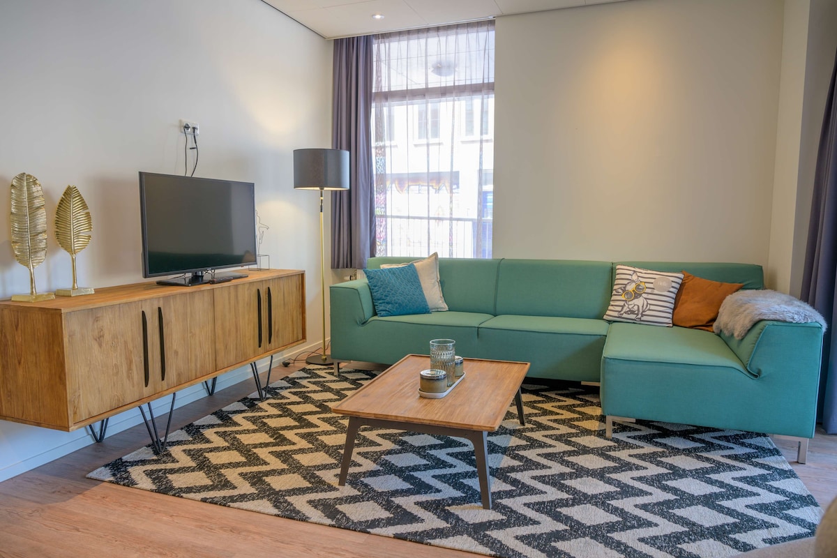 A modern living room with a flat-screen TV, a wooden cabinet, a green sofa, and a patterned rug.