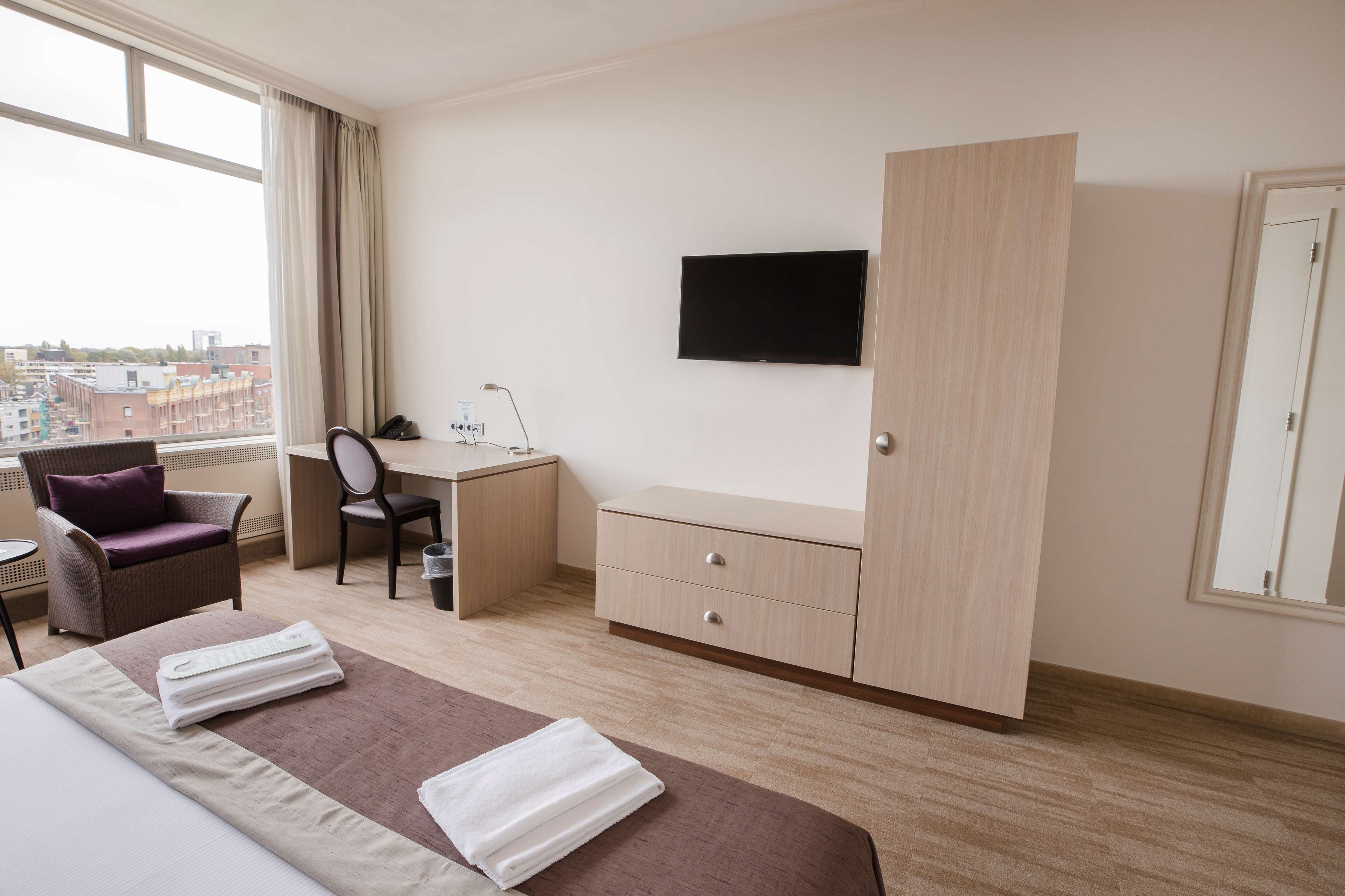 Una habitación de hotel con cama, escritorio, silla, televisor y armario.