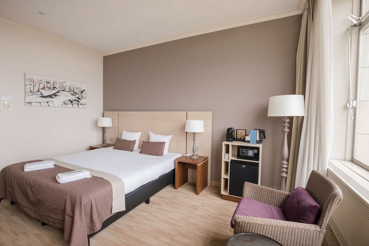A hotel room with a large bed, bedside tables, a chair, a desk, and a window with curtains.