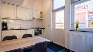 A modern kitchen with white cabinets, a wooden dining table, and a view of a brick building through a window. - Flonk Hotel Groningen Centre, BW Signature Collection (Groningen)