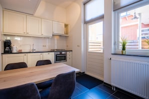 A modern kitchen with white cabinets, a wooden dining table, and a view of a brick building through a window.