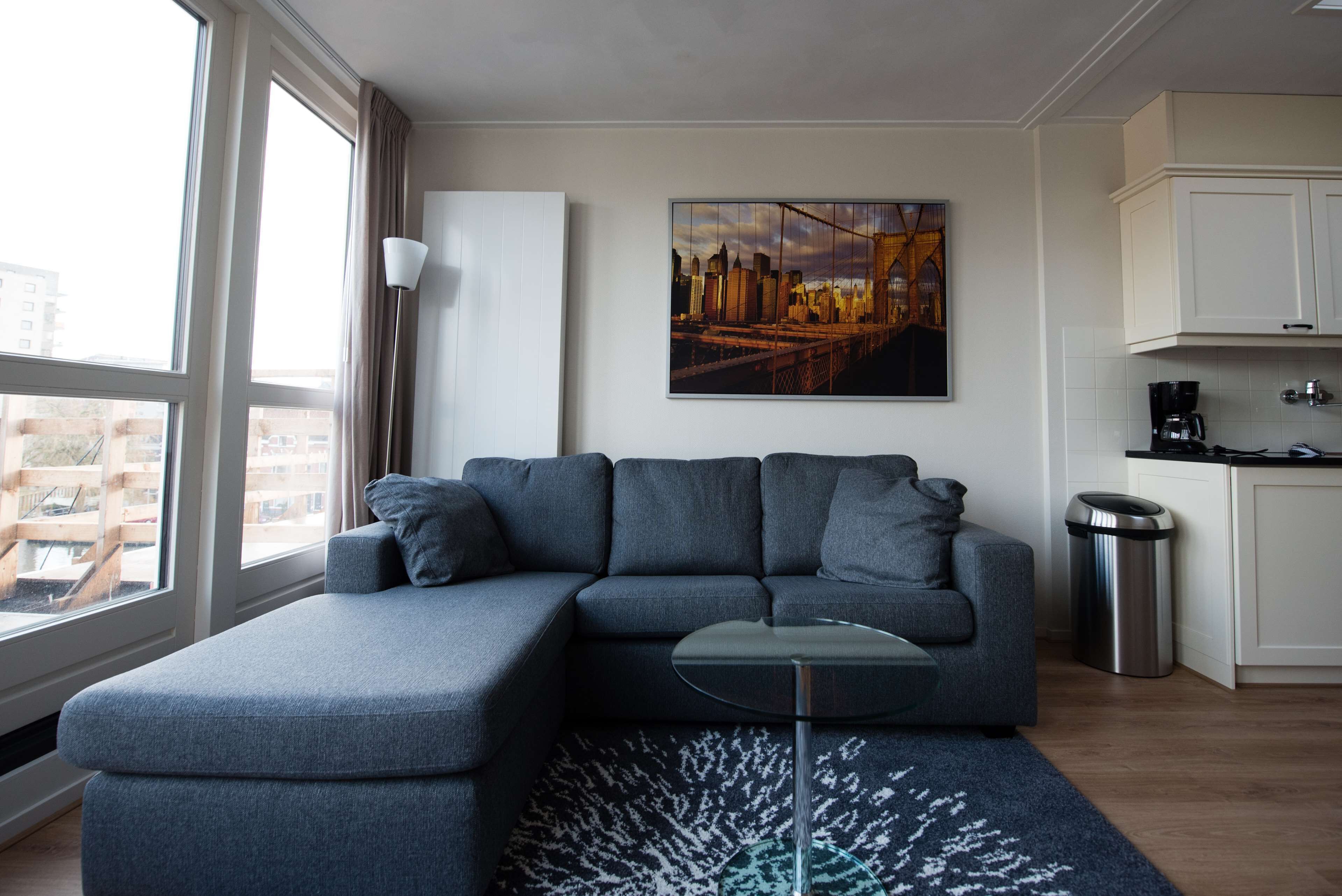 Uma sala de estar moderna com um sofá modular cinza, uma mesa de centro de vidro e uma pintura com vista para a cidade na parede.