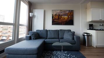 Uma sala de estar moderna com um sofá modular cinza, uma mesa de centro de vidro e uma pintura com vista para a cidade na parede.