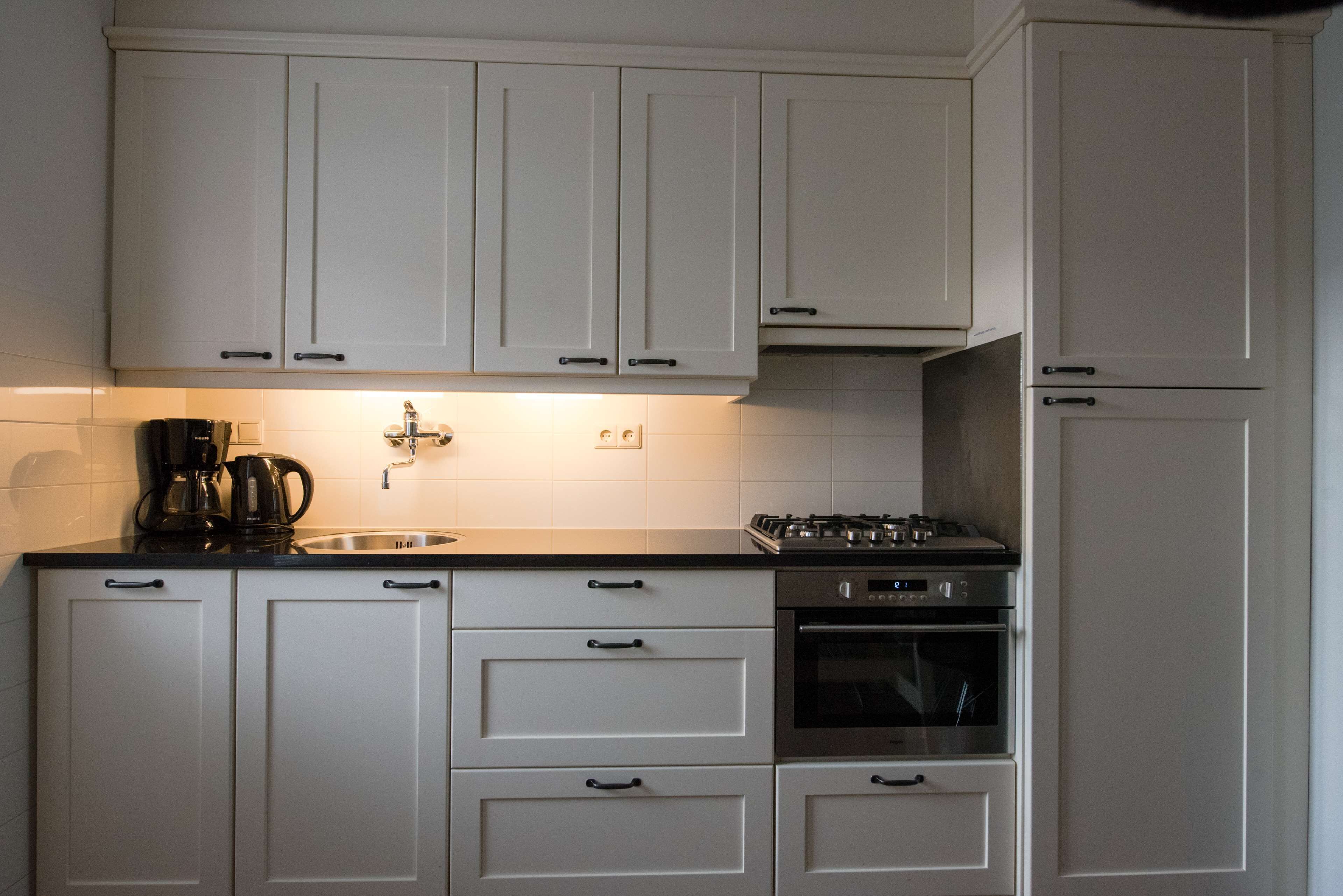 A kitchen with white cabinets, a coffee maker, a sink, and a stove.