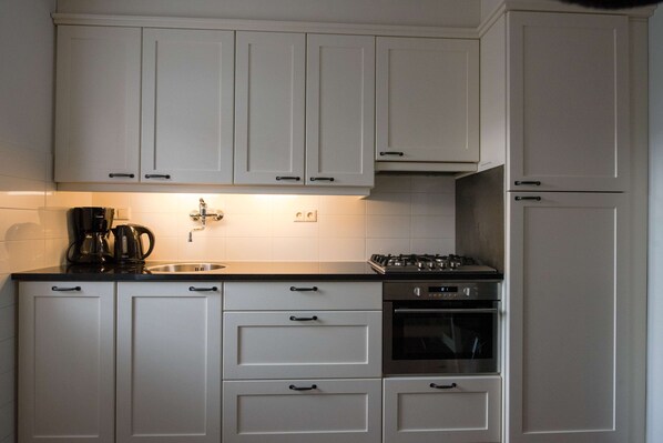 A kitchen with white cabinets, a coffee maker, a sink, and a stove. - Flonk Hotel Groningen Centre, BW Signature Collection (Groningen)