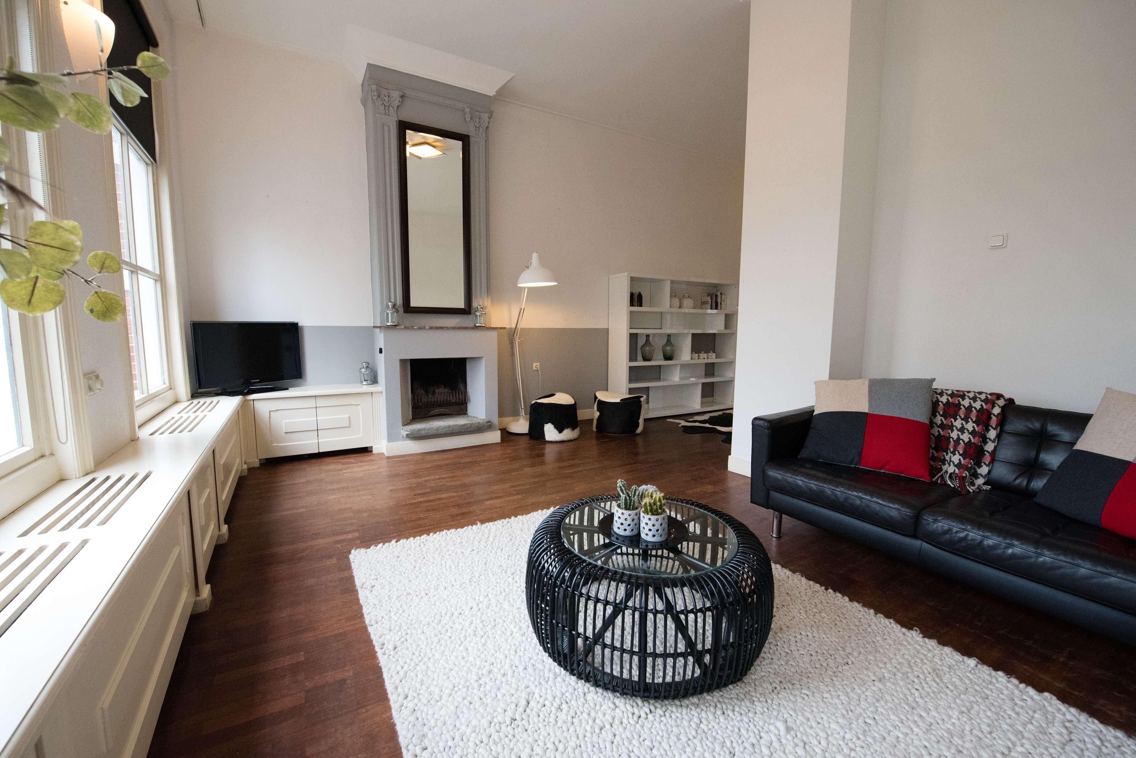 Una sala de estar con chimenea, un sofá de cuero negro, un radiador blanco y un televisor.
