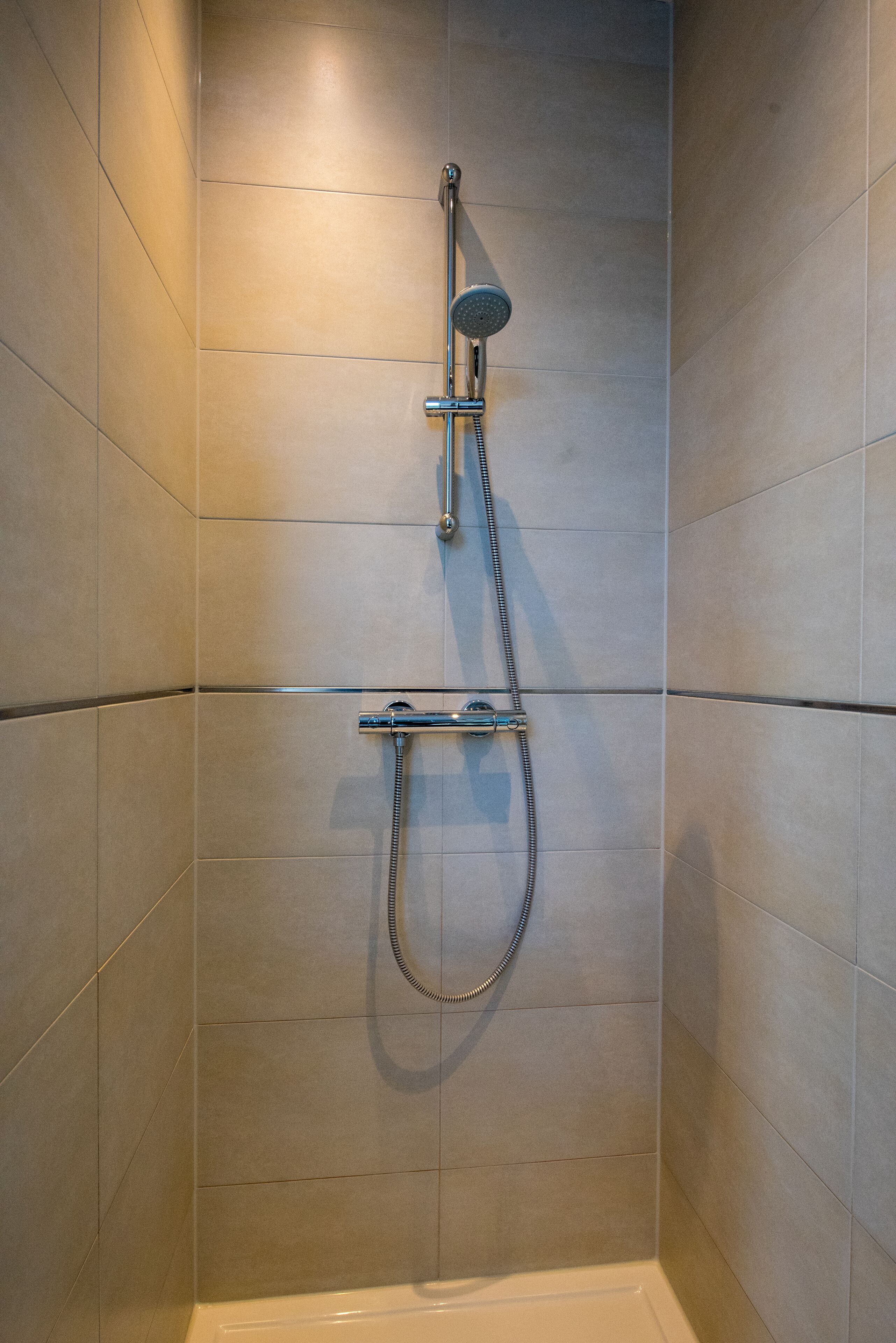 A shower with a handheld showerhead and a fixed wall-mounted showerhead in a tiled room.