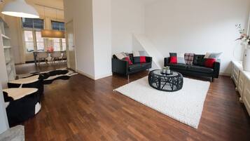 A modern living room with a black sofa, white rug, and a coffee table.