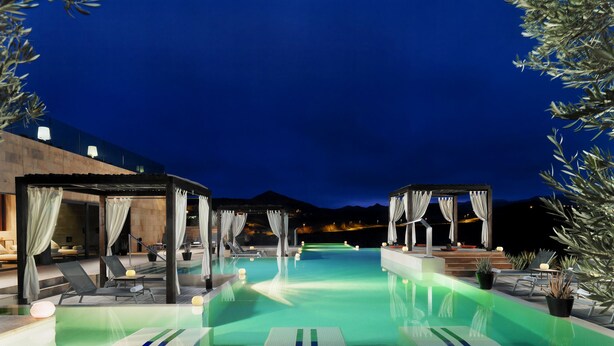 A nighttime swimming pool area with lounge chairs and umbrellas, surrounded by potted plants and a wooden deck. - Villas Salobre (San Bartolome de Tirajana)