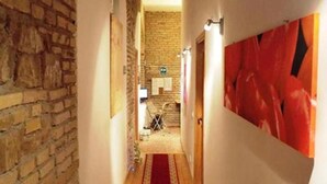 A narrow hallway with a red carpet, stone walls, and a wooden floor.
