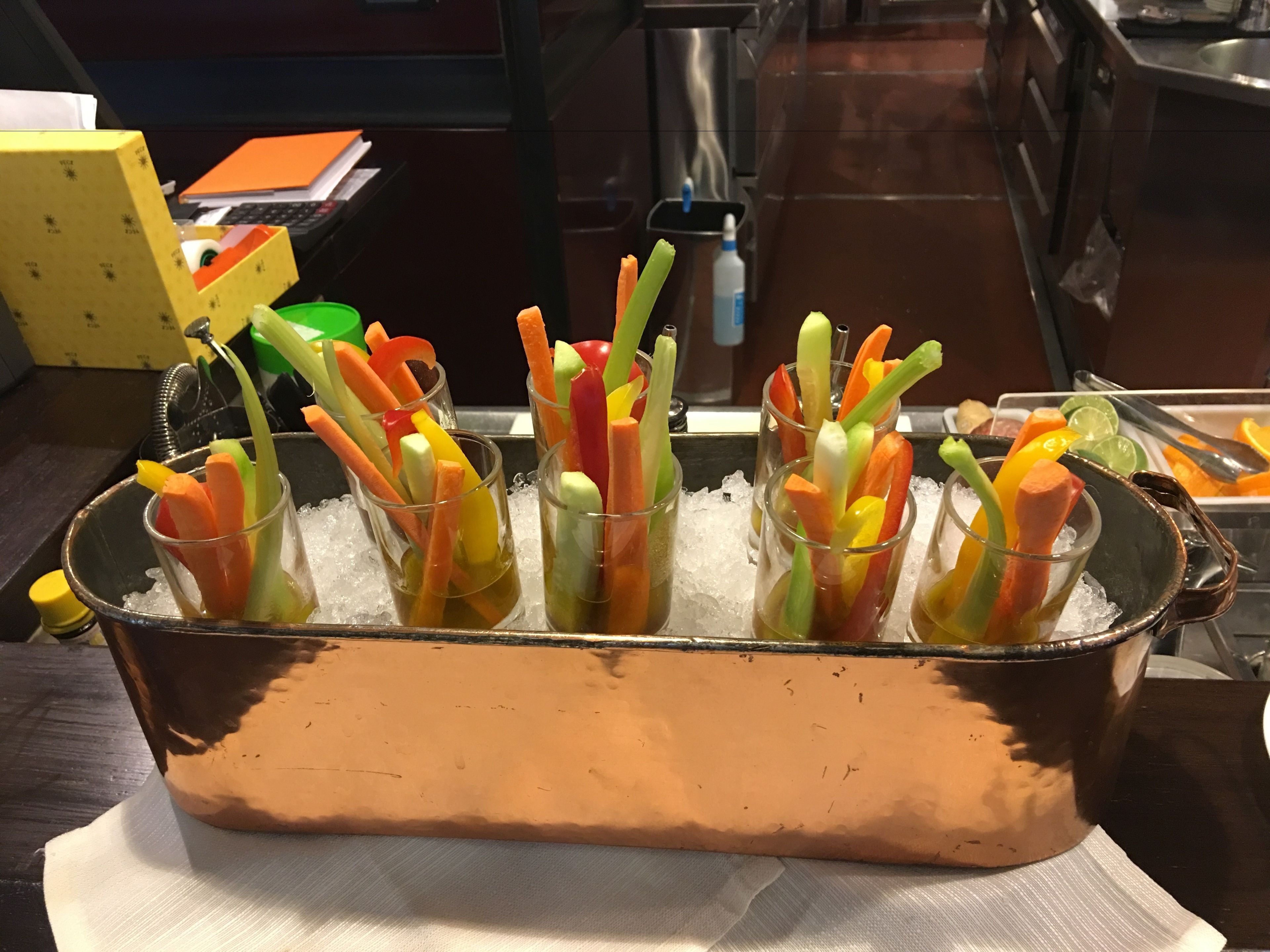 A copper pot filled with ice and containing several glasses of colorful vegetable sticks.