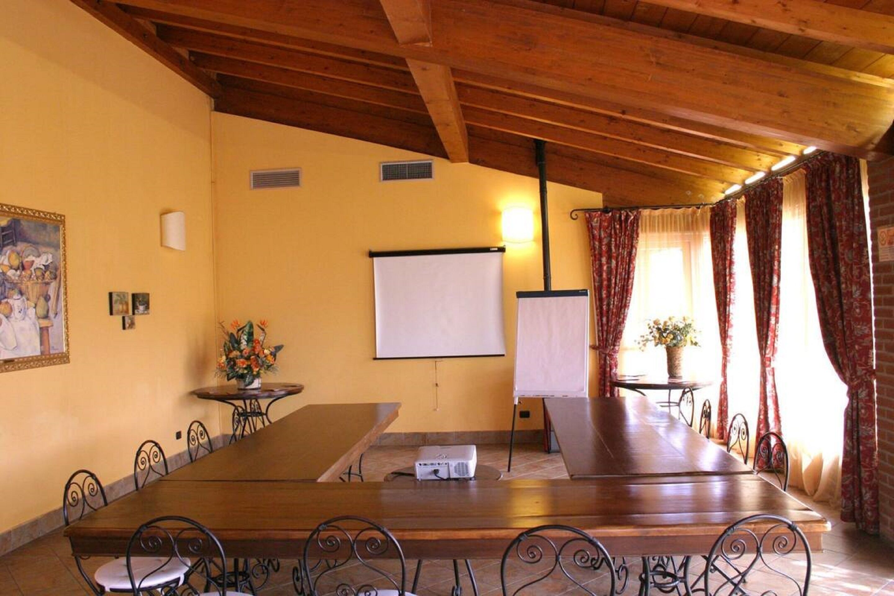 Un salón de conferencias con una larga mesa, sillas, un proyector, una pizarra y un ventanal con cortinas.