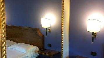 Habitación de hotel con un espejo grande, una cama con ropa blanca, dos mesitas de noche con lámparas y un cabecero de madera.