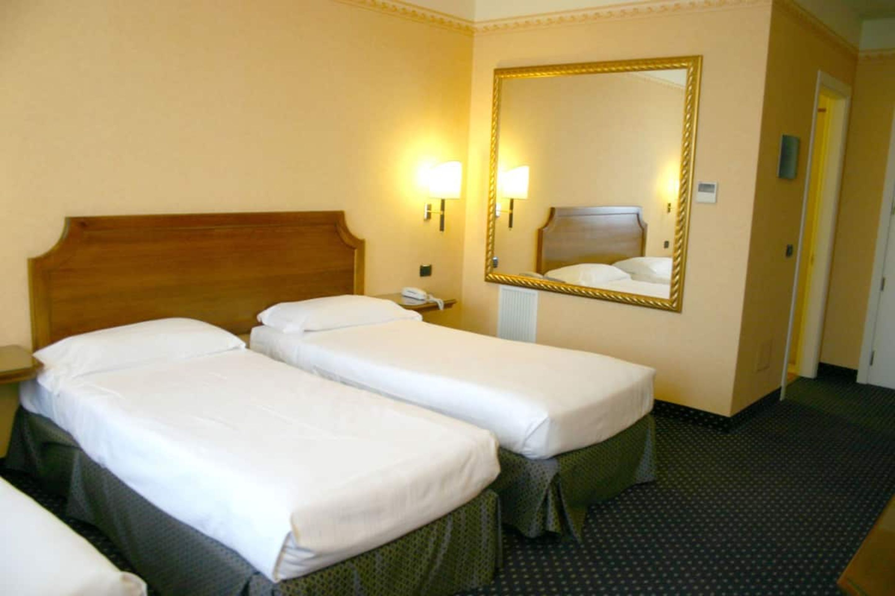 Ein Hotelzimmer mit zwei Einzelbetten, einem Holz-Kopfteil, einem großen Spiegel und einem Telefon auf dem Nachttisch.