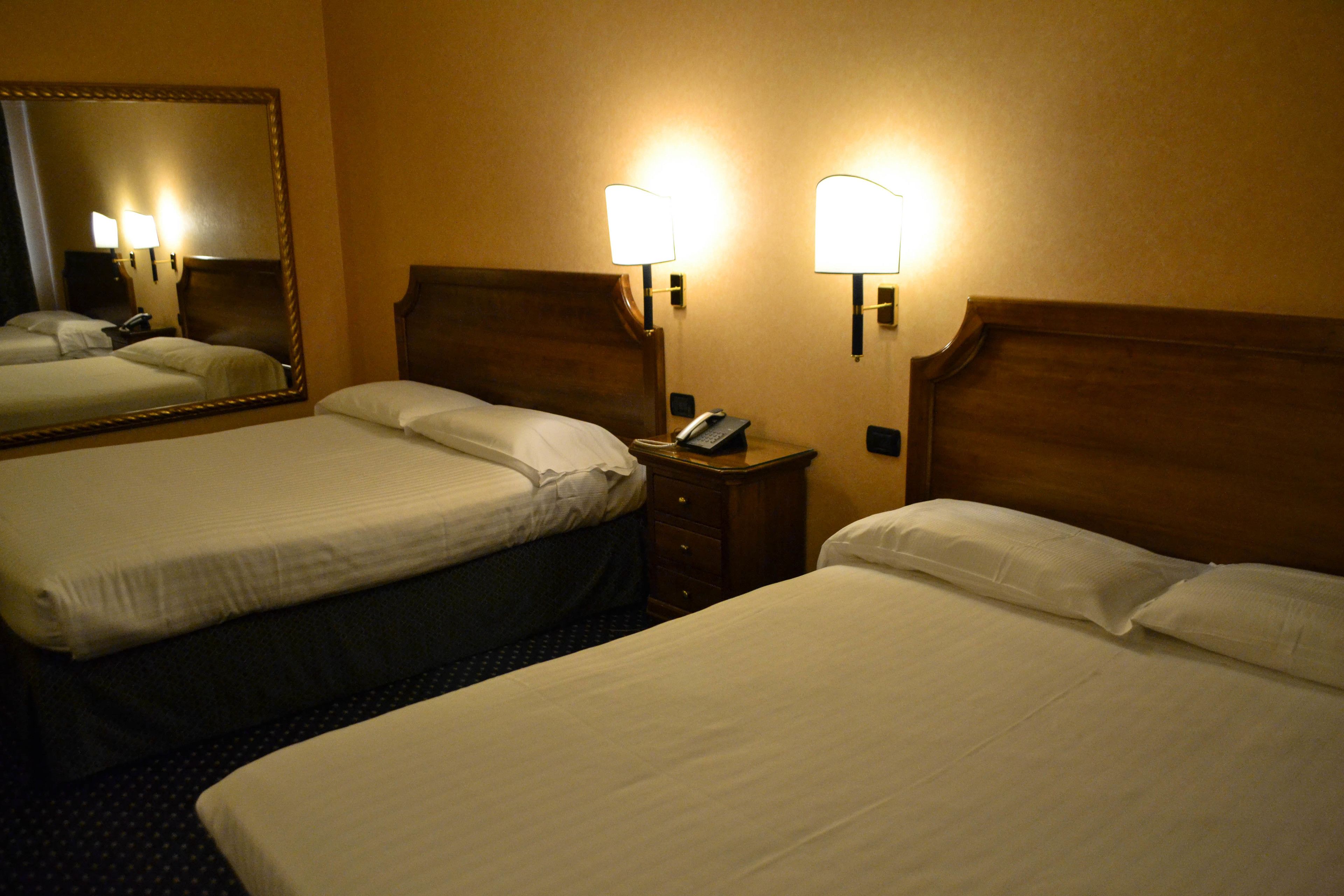 Ein Hotelzimmer mit zwei Betten, einem großen Spiegel, Nachttischlampen und einem Telefon auf einem Nachttisch.