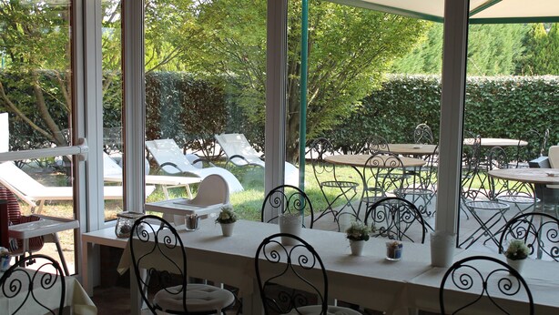 An outdoor dining area with tables and chairs, a covered section with a table, and a view of the garden. - Hotel Don Carlo (Broni)